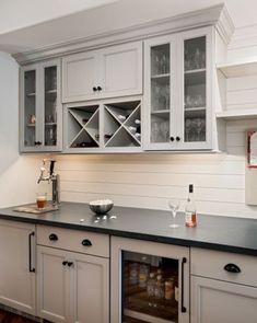 a kitchen with white cabinets and black counter tops, wine glasses on the cabinet doors