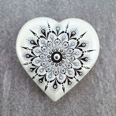 a white heart shaped dish with black and white designs on the front, sitting on a gray surface