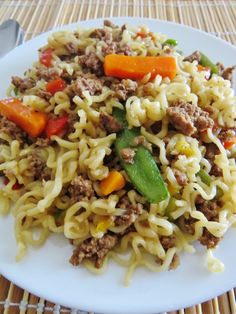 a white plate topped with noodles and meat on top of a wooden table next to a fork