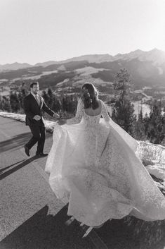 a bride and groom walking down the road in black and white with mountains in the background