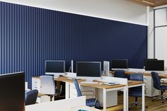 an office with multiple desks and computers on them in front of a blue wall