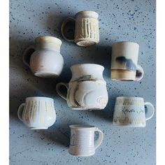 five white coffee mugs sitting next to each other on a blue counter top with one cup in the middle