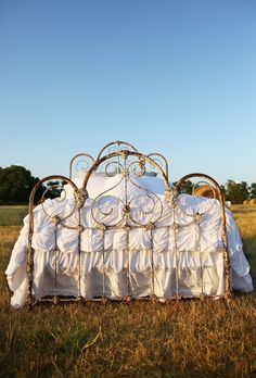 an old iron bed in the middle of a field with white sheets and ruffled bedspread