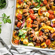 a pan filled with meat and vegetables on top of a white table next to parsley