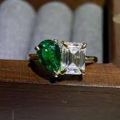 an emerald and diamond ring sitting on top of a wooden table