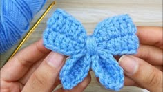 a person holding a blue crocheted bow in their hand next to a ball of yarn