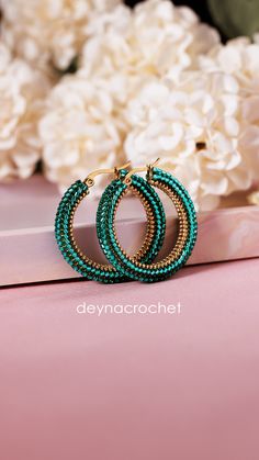 a pair of green beaded hoop earrings sitting on top of a pink table next to white flowers