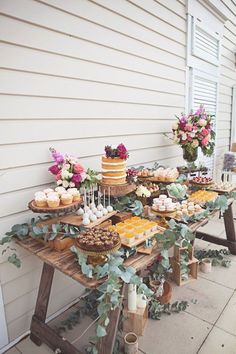 a table with cakes and cupcakes on it in front of a white house