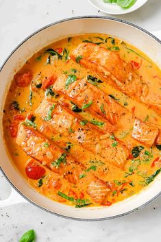 a pan filled with chicken and tomatoes on top of a table next to a bowl of basil