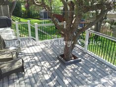 a deck with chairs and a tree in the middle, overlooking a backyard area that is fenced off