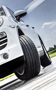 the front end of a white porsche cayenne parked on a road with grass in the background