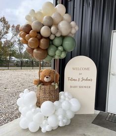 a teddy bear sitting in a basket with balloons attached to it and a welcome sign