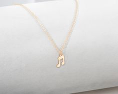 a gold necklace with a musical note charm on it's link, sitting on top of a white pillow