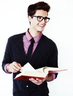 a young man in glasses is holding an open book and smiling at the camera while standing against a white background