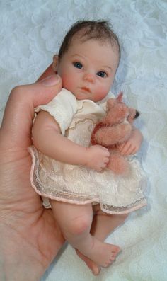 a hand holding a baby doll with a teddy bear