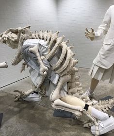 two mannequins dressed in white are standing next to a large dinosaur skeleton