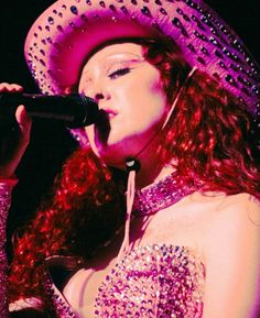 a woman with red hair wearing a hat and singing into a microphone