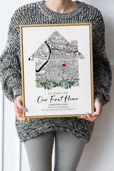 a woman holding up a framed poster with the words, our first home on it