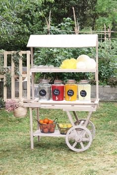 an outdoor cart with fruit and drinks on it in the grass next to some trees