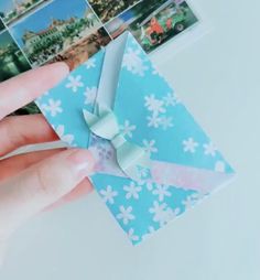 a hand holding an origami bow with pictures on the wall in the background