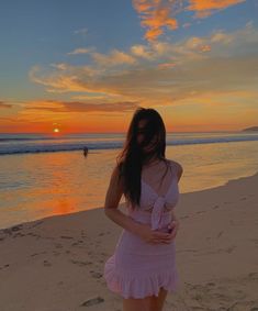 a woman standing on top of a sandy beach next to the ocean at sun set