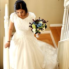 a woman in a wedding dress is walking down the stairs with her bouquet on her hand