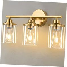 three light bathroom fixture with clear glass shades and gold metal finish, on a white wall