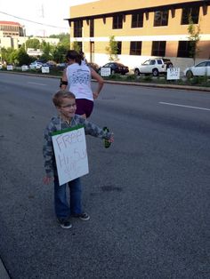 a young boy holding a sign in the middle of the street with other people behind him