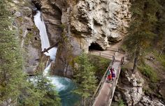 people walking across a bridge over a river in the woods next to tall rocks and trees