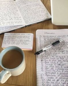 a cup of coffee sitting on top of a wooden table next to an open notebook