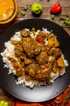 a black plate topped with rice and meat covered in gravy on top of a wooden table