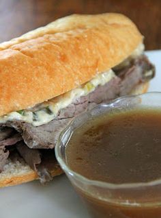 a roast beef sandwich with gravy on a plate next to a cup of soup