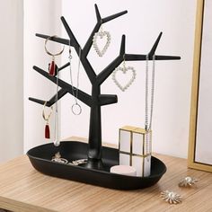 a black tree with jewelry hanging from it's branches on a table next to a mirror