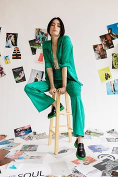 a woman sitting on top of a wooden stool in front of a wall covered with pictures