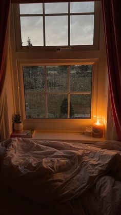 a bedroom with a window and a bed in front of the window is lit by a candle