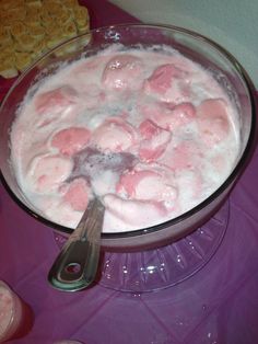 a bowl filled with pink jello next to crackers on a purple table cloth