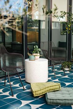 two chairs and a table on a tiled floor in front of a glass window with potted plants