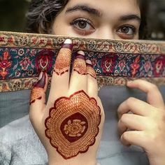 a close up of a person with henna on their hand and holding something in front of her face