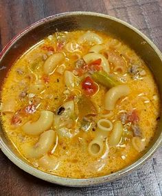 a metal bowl filled with pasta soup on top of a wooden table