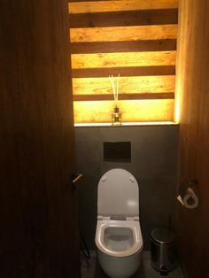 a white toilet sitting inside of a bathroom next to a wooden wall with lights on it