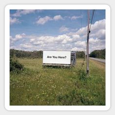 a sign that says are you here? in the middle of a field with power lines