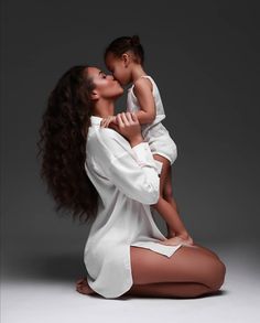 a woman sitting on the ground holding a baby in her lap and kissing her cheek