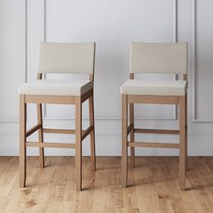 two wooden stools sitting side by side on a hard wood floor in front of a white wall