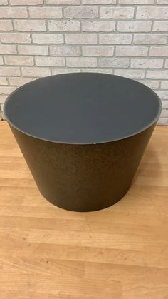 a large black bowl sitting on top of a wooden table next to a brick wall