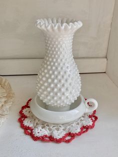 a white vase sitting on top of a table next to a red and white doily