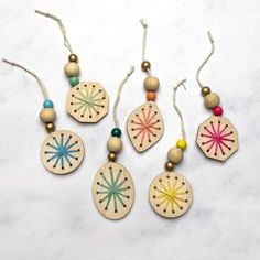 four wooden ornaments with beads and string on a marble surface, one is decorated with flowers