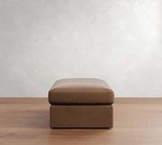 a brown ottoman sitting on top of a hard wood floor next to a white wall