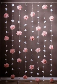 pink and white paper flowers are hanging from a string in front of a brown wall