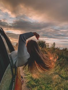 a woman leaning out the window of a car with her hair blowing in the wind