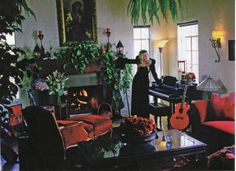 a woman standing in a living room next to a piano and potted plant on the table